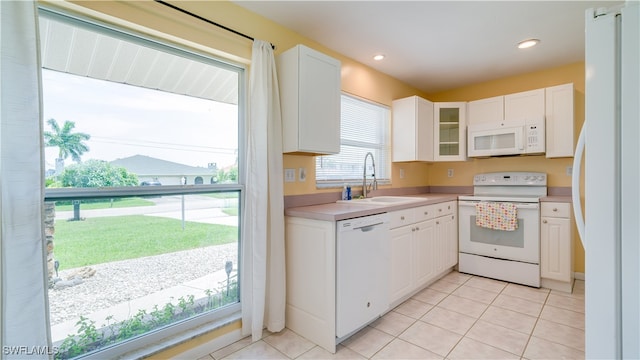 kitchen with white cabinetry, sink, light tile patterned floors, and white appliances