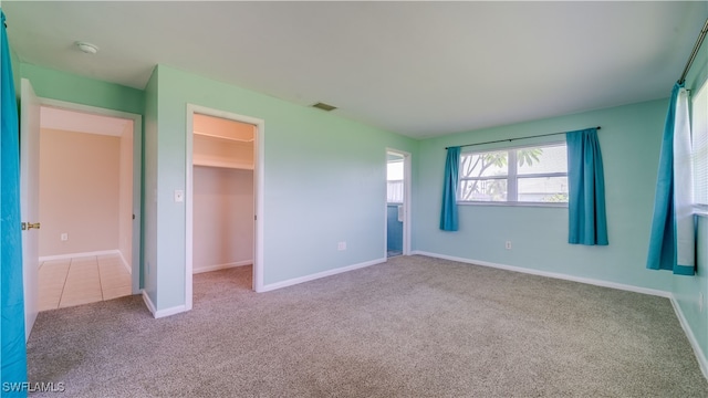 unfurnished bedroom with a walk in closet, light carpet, and a closet