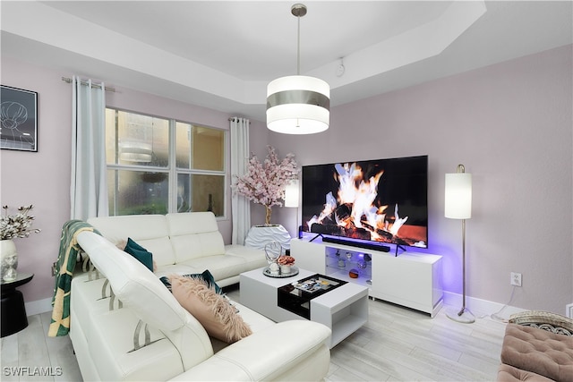 living room with light wood-type flooring and a raised ceiling