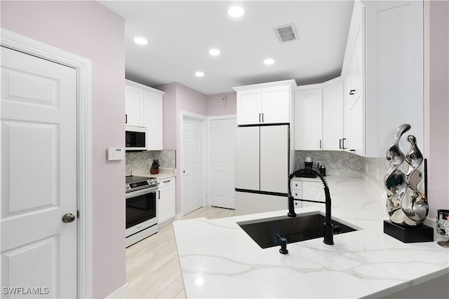 kitchen featuring white fridge, light stone counters, stainless steel electric range, and white cabinets