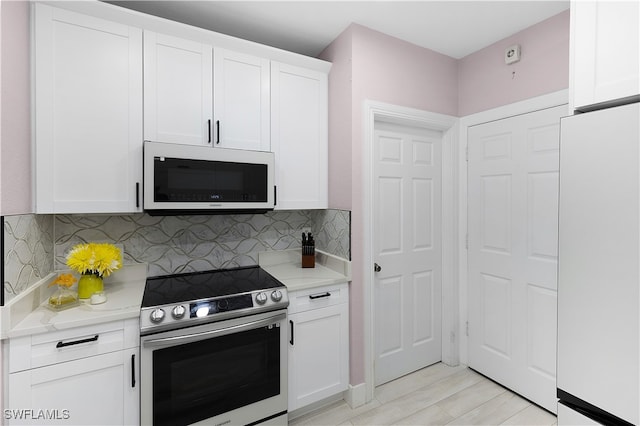 kitchen featuring light wood-type flooring, stainless steel range with electric stovetop, white cabinets, white fridge, and decorative backsplash