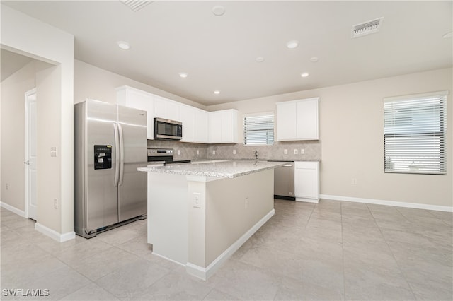 kitchen featuring decorative backsplash, stainless steel appliances, a center island, white cabinets, and light stone counters