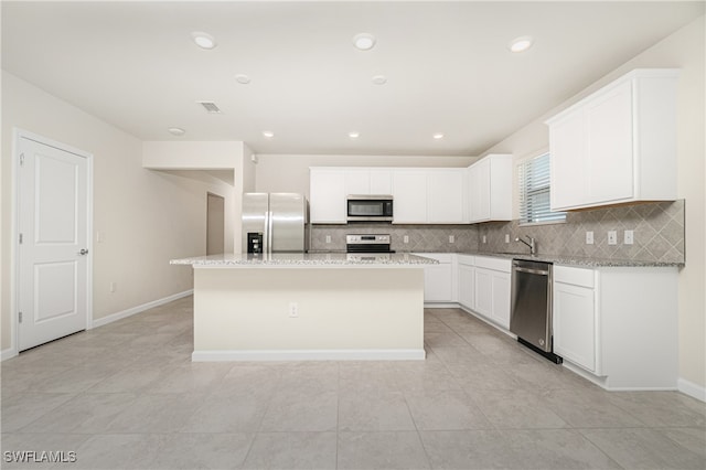 kitchen with light stone countertops, appliances with stainless steel finishes, a kitchen island, white cabinetry, and decorative backsplash