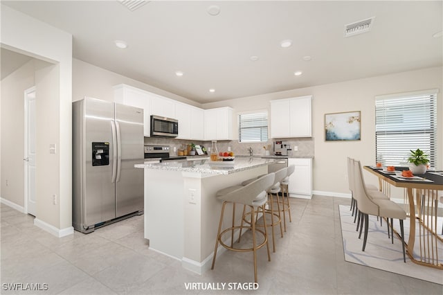 kitchen featuring appliances with stainless steel finishes, white cabinetry, backsplash, and a kitchen island