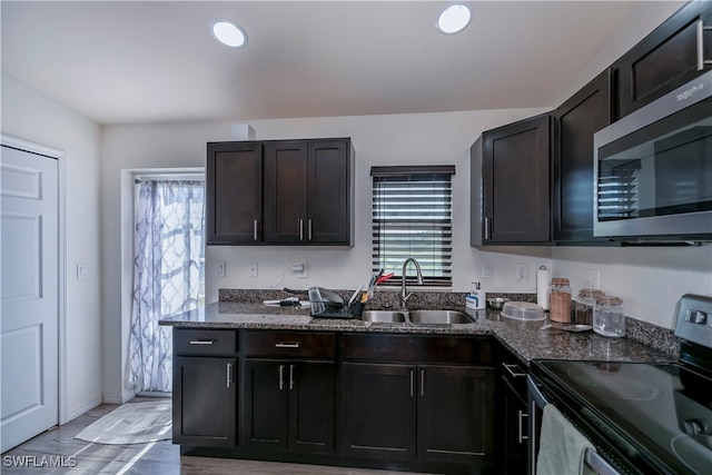 kitchen featuring wood-type flooring, dark stone counters, sink, dark brown cabinetry, and appliances with stainless steel finishes