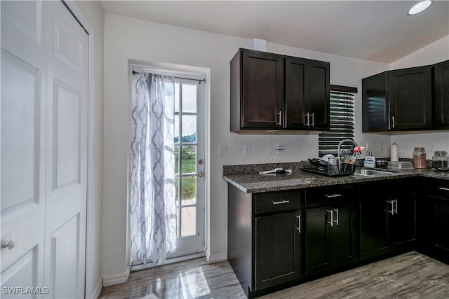 kitchen featuring sink, dark brown cabinetry, light wood-type flooring, and dark stone counters