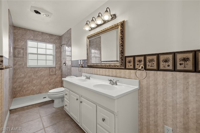 bathroom with tiled shower, tile patterned floors, toilet, tile walls, and vanity