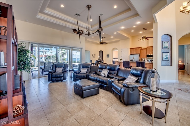 tiled living room featuring ceiling fan with notable chandelier, a towering ceiling, and a raised ceiling