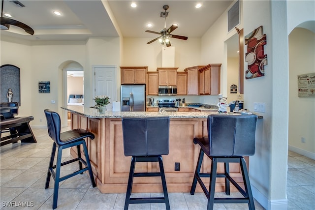 kitchen featuring kitchen peninsula, a kitchen breakfast bar, stainless steel appliances, and light stone countertops