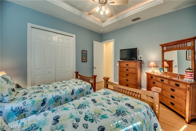 bedroom with a raised ceiling, ceiling fan, crown molding, light hardwood / wood-style floors, and a closet