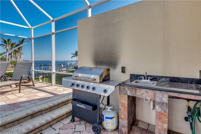 view of patio featuring area for grilling, sink, a water view, and glass enclosure