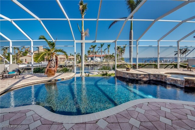 view of pool featuring an in ground hot tub, a water view, glass enclosure, and a patio area