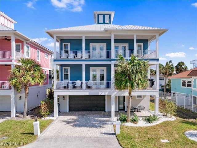 coastal home featuring decorative driveway, a standing seam roof, metal roof, fence, and a garage