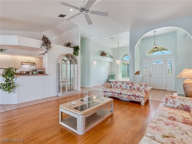 living room featuring lofted ceiling, ceiling fan with notable chandelier, light wood-type flooring, and a wealth of natural light