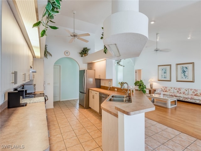 kitchen with kitchen peninsula, stainless steel appliances, sink, light tile patterned floors, and high vaulted ceiling