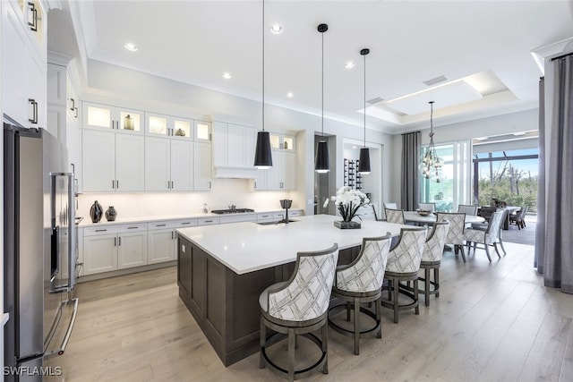 kitchen featuring an island with sink, stainless steel fridge, white cabinets, and pendant lighting