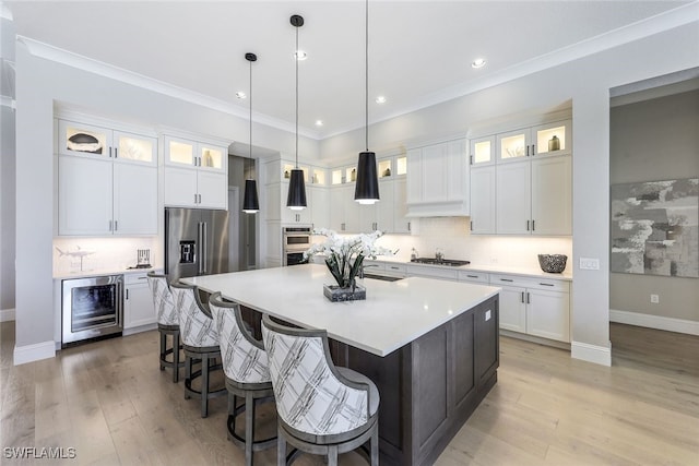 kitchen with an island with sink, hanging light fixtures, white cabinetry, light hardwood / wood-style floors, and beverage cooler