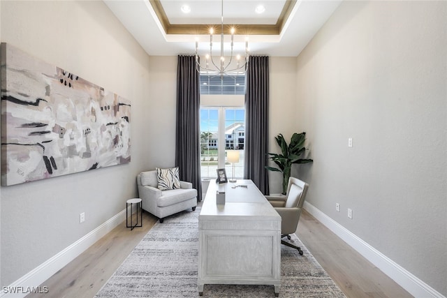 office with light hardwood / wood-style floors, a tray ceiling, and an inviting chandelier