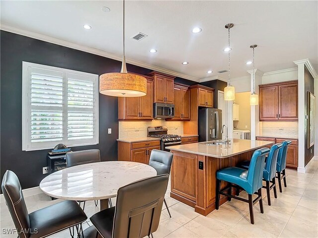 kitchen featuring hanging light fixtures, appliances with stainless steel finishes, a kitchen breakfast bar, an island with sink, and backsplash