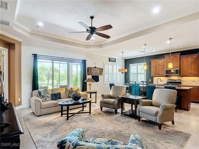 tiled living room with a raised ceiling, crown molding, sink, and ceiling fan