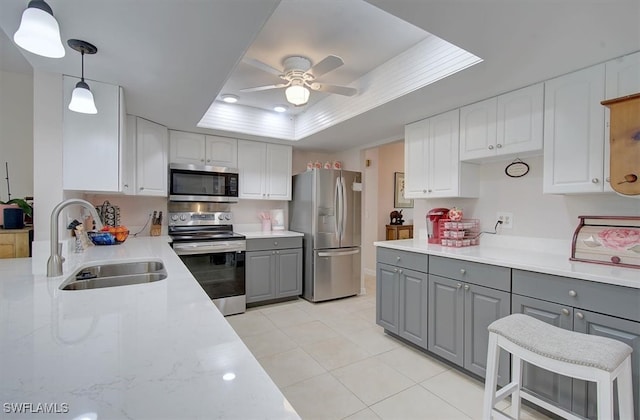 kitchen with gray cabinets, stainless steel appliances, pendant lighting, and a raised ceiling