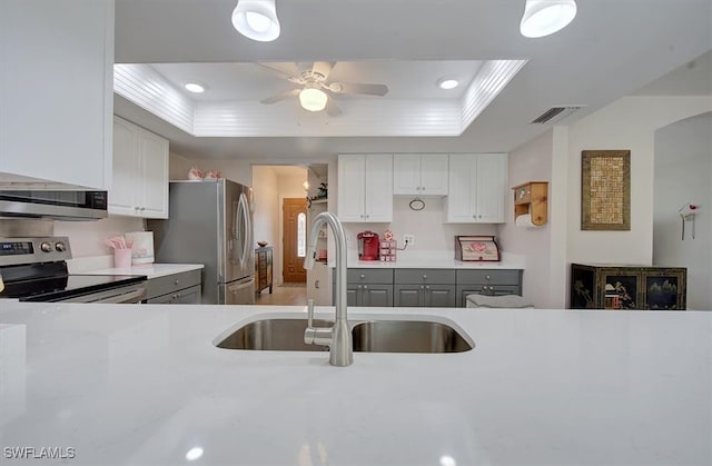 kitchen featuring white cabinets, a raised ceiling, appliances with stainless steel finishes, gray cabinets, and sink