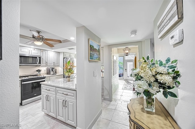 kitchen with appliances with stainless steel finishes, light stone counters, light tile patterned floors, and ceiling fan