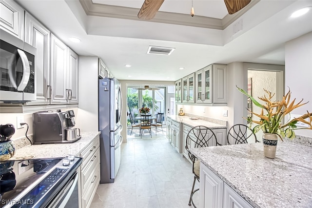 kitchen with a kitchen breakfast bar, stainless steel appliances, a tray ceiling, light stone counters, and ceiling fan