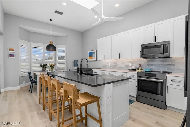 kitchen featuring pendant lighting, a breakfast bar, white cabinets, a center island with sink, and stainless steel range with electric cooktop