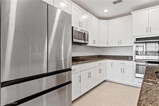 kitchen with appliances with stainless steel finishes, white cabinetry, and dark stone countertops