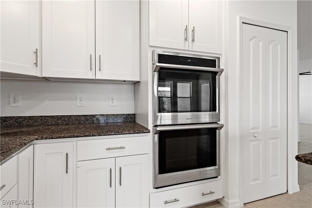 kitchen with white cabinetry, dark stone countertops, light tile patterned floors, and stainless steel double oven