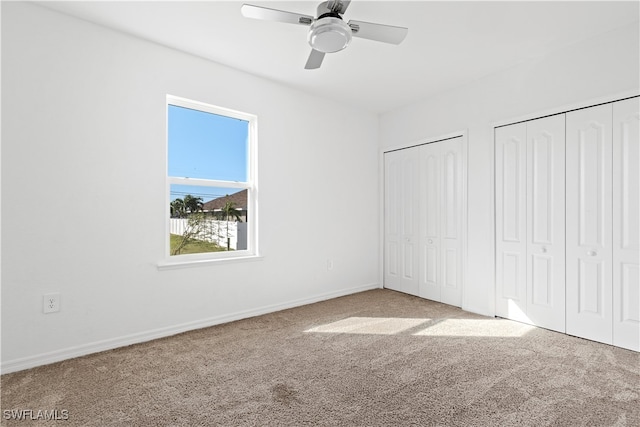 unfurnished bedroom featuring ceiling fan, carpet floors, and two closets