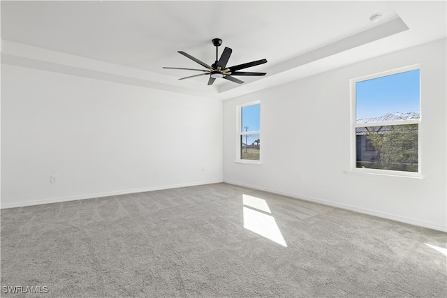 carpeted empty room featuring ceiling fan, a tray ceiling, and a wealth of natural light