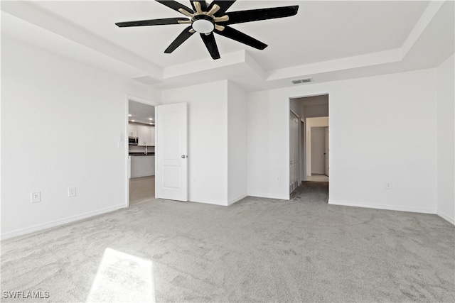 unfurnished bedroom featuring a spacious closet, light carpet, a tray ceiling, and ceiling fan