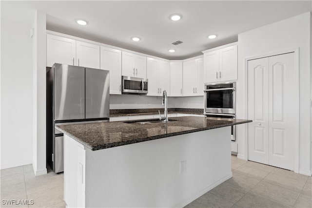 kitchen featuring a center island with sink, white cabinets, stainless steel appliances, and dark stone counters