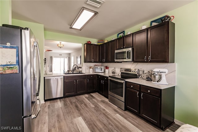 kitchen with dark brown cabinetry, stainless steel appliances, sink, and light hardwood / wood-style flooring