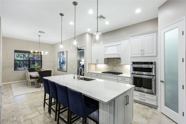 kitchen featuring sink, a center island with sink, custom range hood, stainless steel appliances, and white cabinets