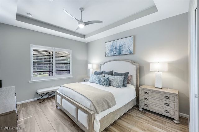 bedroom featuring a raised ceiling, ceiling fan, and light hardwood / wood-style floors