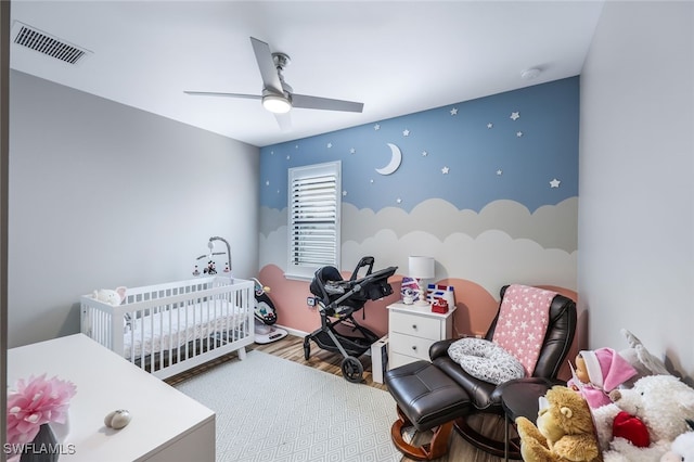 bedroom featuring wood-type flooring, a nursery area, and ceiling fan