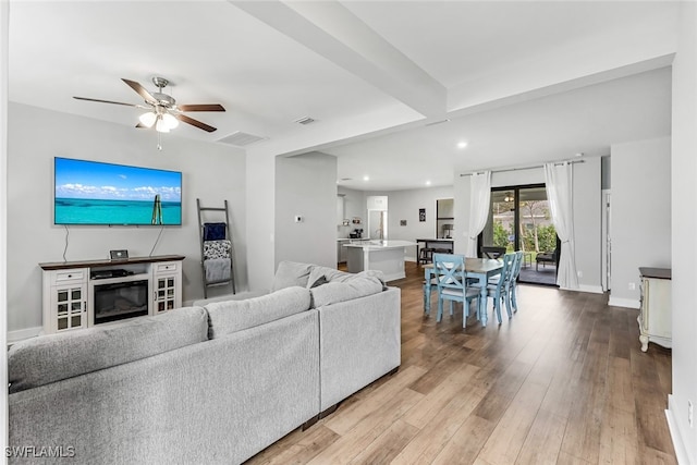 living room featuring beamed ceiling, wood-type flooring, and ceiling fan