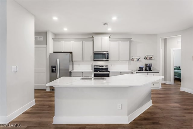 kitchen featuring light stone countertops, appliances with stainless steel finishes, sink, dark hardwood / wood-style flooring, and a kitchen island with sink