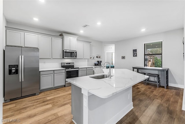 kitchen with light hardwood / wood-style flooring, an island with sink, gray cabinetry, sink, and appliances with stainless steel finishes