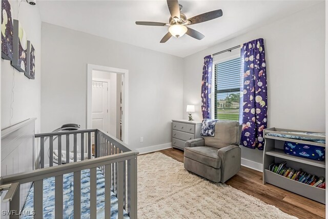 bedroom with ceiling fan, wood-type flooring, and a nursery area