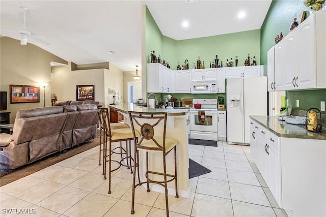 kitchen with white appliances, light tile patterned floors, vaulted ceiling, white cabinets, and a breakfast bar