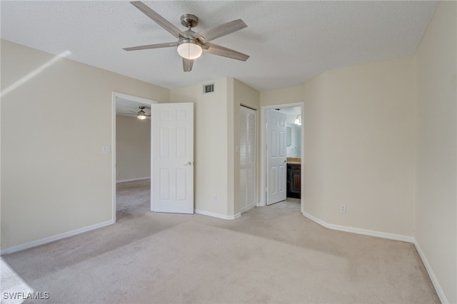 unfurnished bedroom featuring a textured ceiling, ensuite bathroom, light colored carpet, and ceiling fan