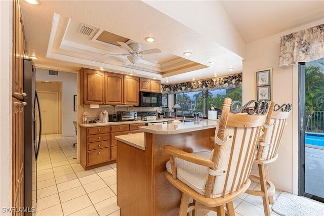 kitchen with appliances with stainless steel finishes, a kitchen bar, backsplash, a raised ceiling, and ceiling fan