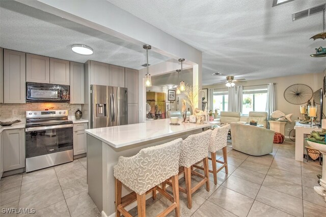 kitchen with an island with sink, gray cabinetry, a kitchen breakfast bar, backsplash, and appliances with stainless steel finishes