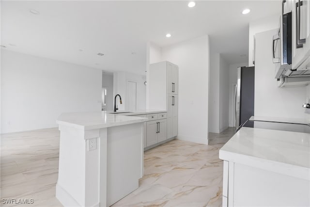 kitchen featuring light stone countertops, appliances with stainless steel finishes, sink, kitchen peninsula, and white cabinets