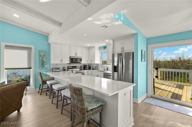 kitchen featuring white cabinets, a kitchen breakfast bar, a wealth of natural light, appliances with stainless steel finishes, and kitchen peninsula