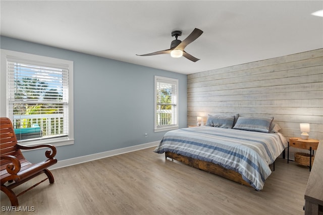 bedroom featuring multiple windows, ceiling fan, wooden walls, and light hardwood / wood-style floors